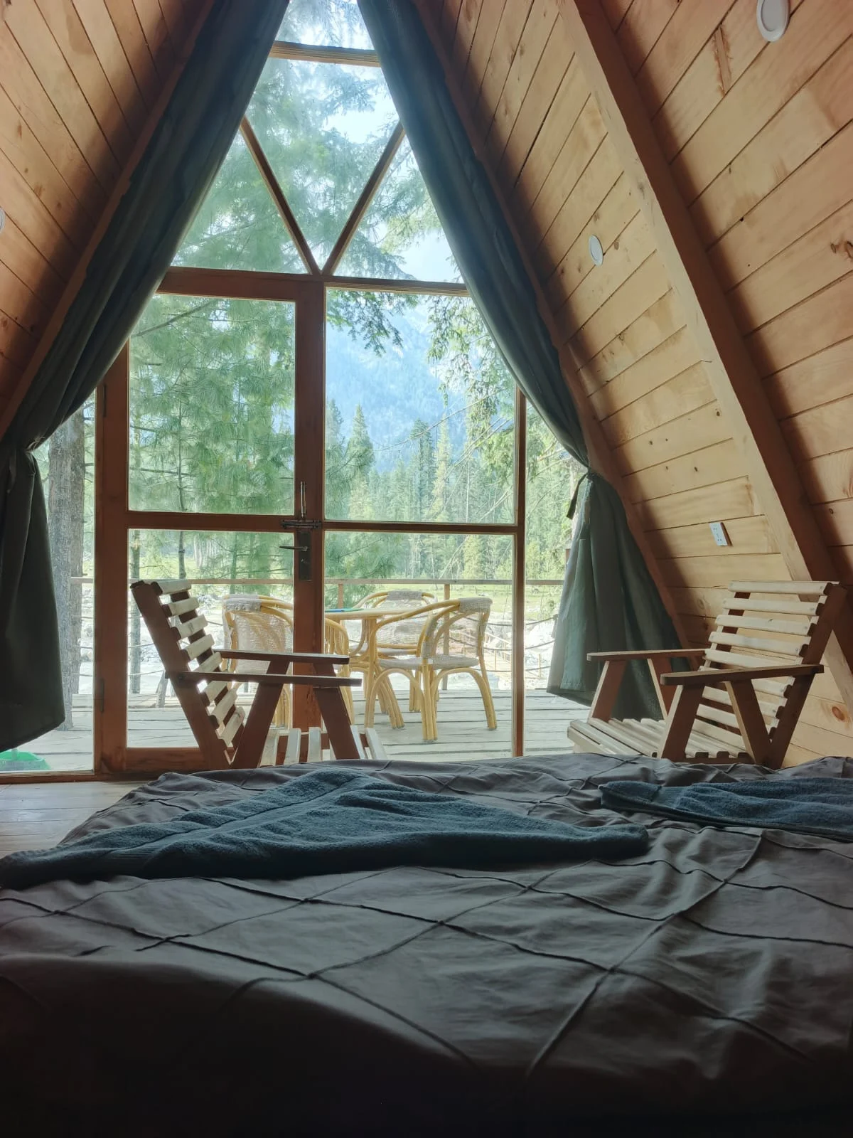 A cozy bed with triangular windows opening onto the forest